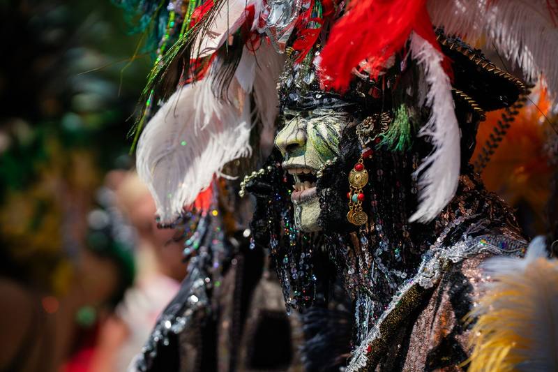 Close-up van een gemaskerde figuur in een kostuum van witte, rode en zwarte veren.